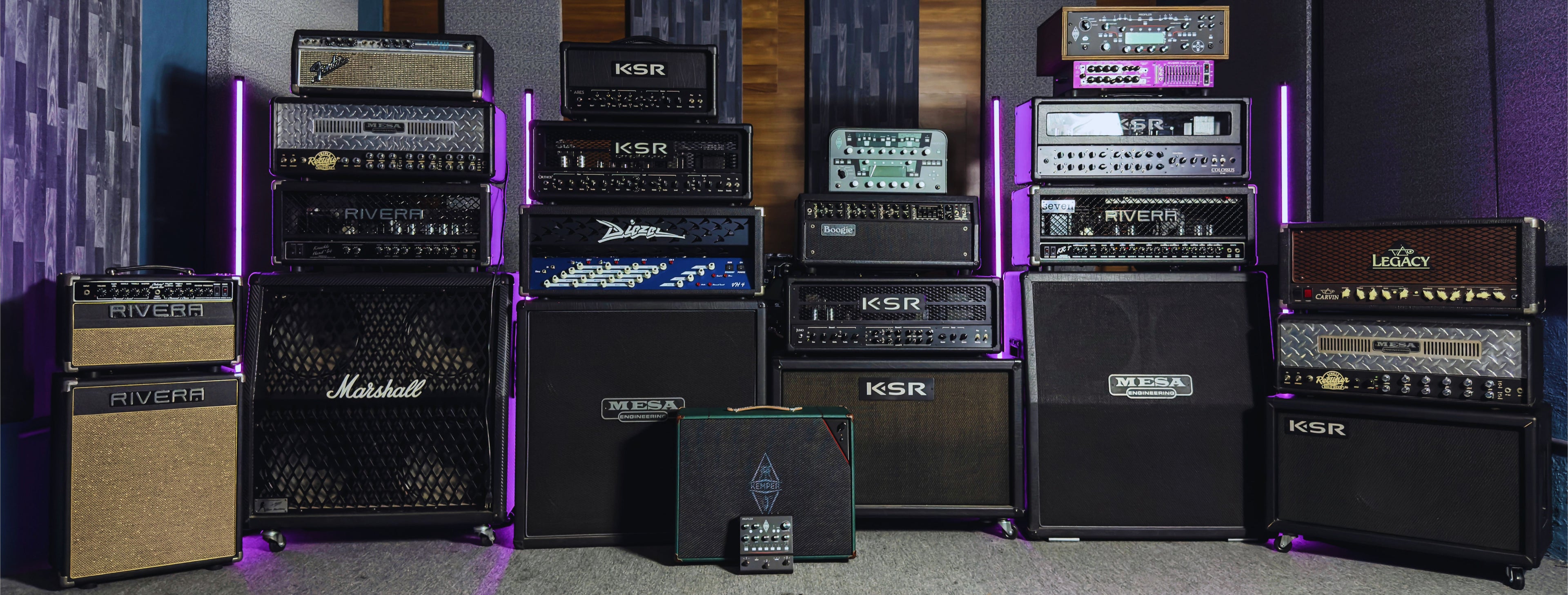 Collection of various guitar amplifiers and speakers arranged against a colorful wall.